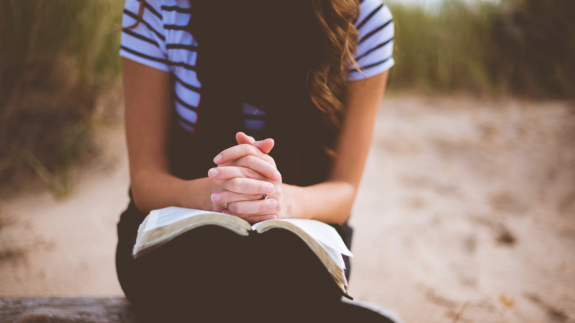 woman-sitting-on-brown-bench-while-reading-book-and-praying