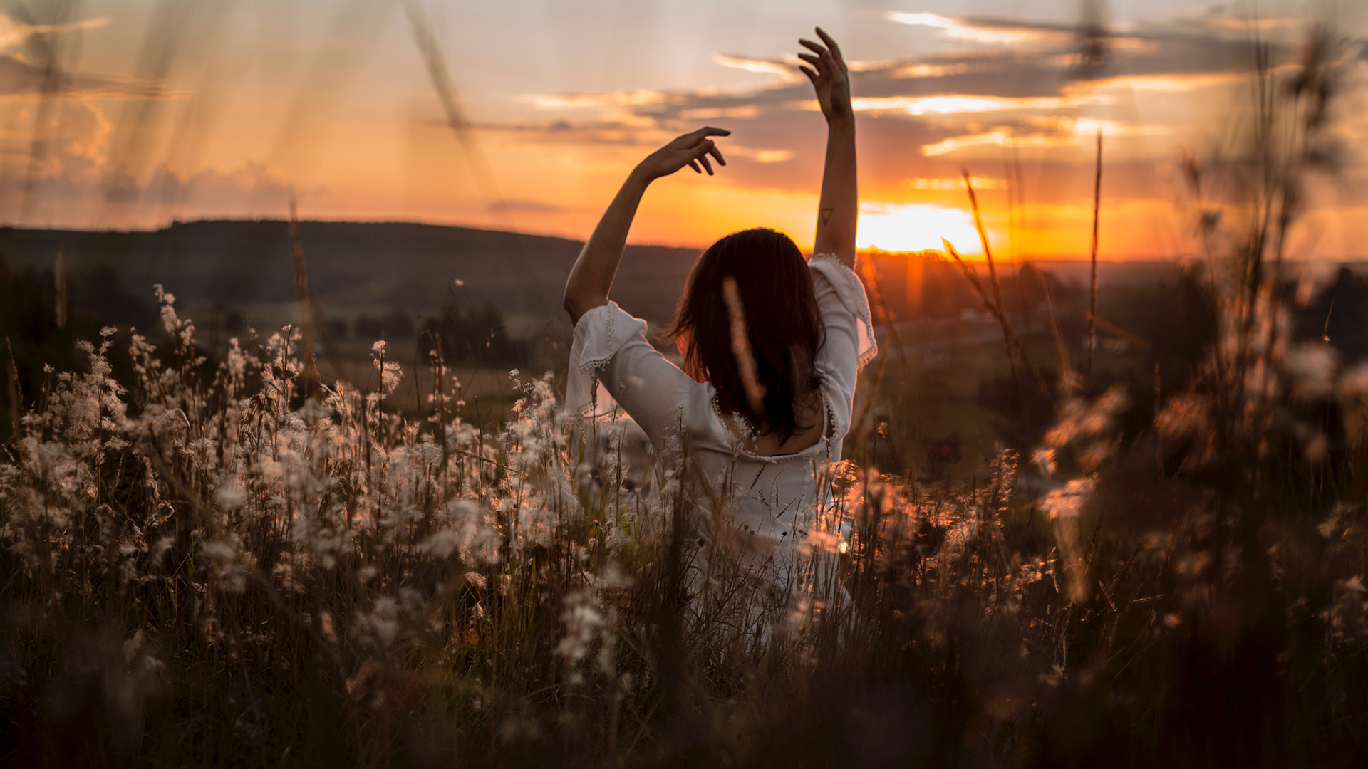 woman-wearing-white-dress-raising-her-two-hands-surrounded-white-petaled-flowers-during-sunset