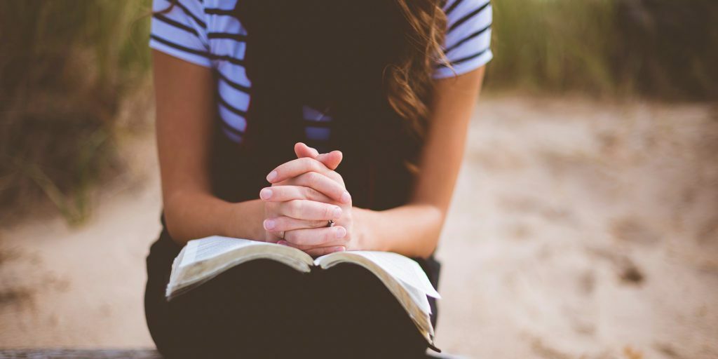 woman-sitting-on-brown-bench-while-reading-book-and-praying